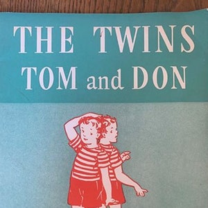 Puede incluir: Una portada de libro vintage con fondo azul y el título "THE TWINS TOM and DON" en letras rojas. La portada también presenta una ilustración de dos niños con camisas a rayas rojas y blancas y pantalones cortos rojos. El texto "EASY GROWTH IN READING" está impreso en negro en la parte inferior de la portada.