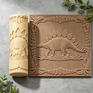 May include: A cylindrical beige rolling pin and a square brown flat stamp, both featuring a raised relief design of a Stegosaurus dinosaur surrounded by a decorative border of stylized leaves and geometric shapes on their surfaces.