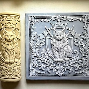 May include: A cylindrical beige rolling pin and a square gray tile, both featuring a raised relief design of a long-haired cat sitting in front of a shield, crossed swords, and a crown, surrounded by intricate scrolling floral and leaf patterns.