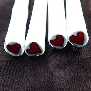 May include: Four white sticks with red heart designs at the end. The hearts are outlined in black.