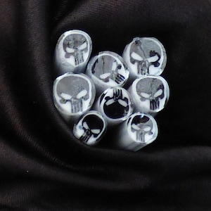 May include: A group of white polymer clay skull beads with a black skull design. The beads are arranged in a heart shape.