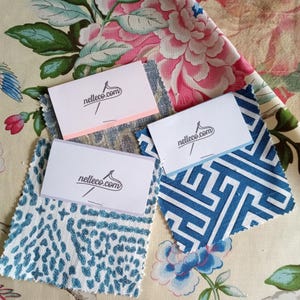 May include: Three fabric swatches in blue and white patterns with business cards that say "nelleco.com" on top of a floral fabric.
