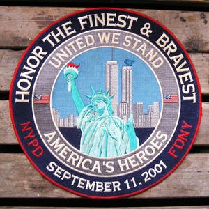 May include: A circular embroidered patch featuring the Statue of Liberty and the Twin Towers against a light blue sky. The border text reads HONOR THE FINEST & BRAVEST, UNITED WE STAND, AMERICA'S HEROES, NYPD, FDNY, and SEPTEMBER 11, 2001.