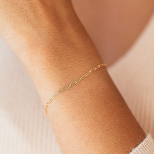 May include: A gold chain bracelet with a delicate, linked design. The bracelet is worn on a person's wrist.
