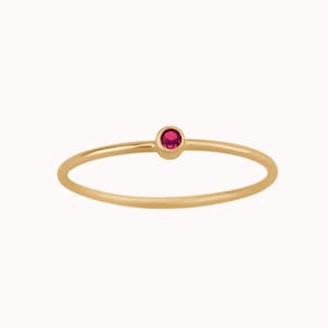 May include: A delicate gold ring with a single, small, red gemstone.