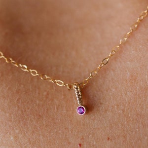 May include: A delicate gold chain necklace with a small pink gemstone pendant.