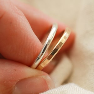 May include: Two thin rings, one silver and one gold, are stacked on top of each other. The gold ring has a textured surface.