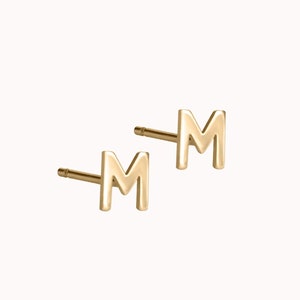 May include: A pair of gold-toned initial earrings featuring the letter "M".