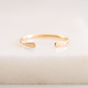 May include: A gold open ring with a hammered finish. The ring is open on one side and has a slightly rounded shape.