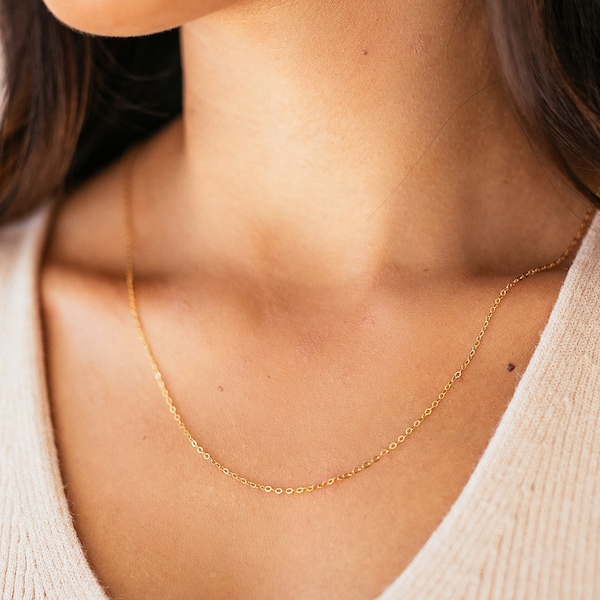 May include: A delicate gold chain necklace worn by a person with a white sweater.