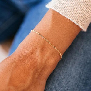May include: A delicate gold chain bracelet on a person's wrist. The bracelet is simple and elegant, perfect for everyday wear.