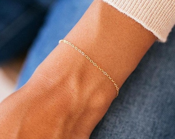 May include: A delicate gold chain bracelet on a person's wrist. The bracelet is simple and elegant, perfect for everyday wear.