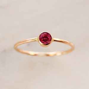 May include: A simple gold band ring with a single, round, dark red gemstone.