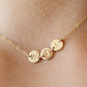 May include: A gold chain necklace with three small round charms, each with a letter engraved on it. The letters are W, J, and A.