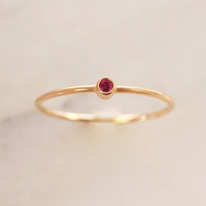 May include: A delicate gold ring with a single, small, red gemstone.