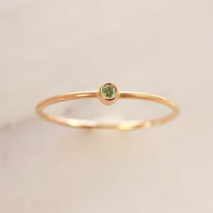 May include: A delicate gold ring with a small green gemstone set in the center.