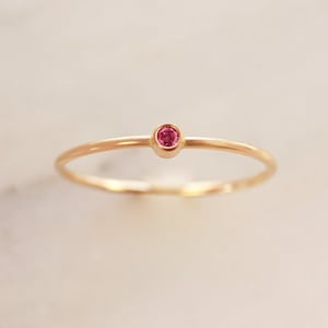 May include: A delicate gold ring with a small, round, pink gemstone.