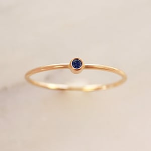 May include: A delicate gold band ring with a small, round blue sapphire gemstone.