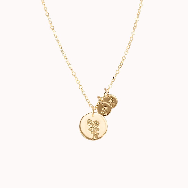 May include: A gold necklace with three charms. The largest charm features a floral design, while the two smaller charms are plain.