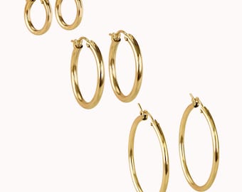 May include: Set of three gold hoop earrings in different sizes. The earrings are made of metal and have a smooth finish.