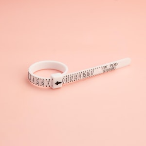May include: White plastic ring sizer with black markings for measuring ring sizes from 0 to 17. The sizer has the text "PAT. PENDO. 9101693" printed on it.