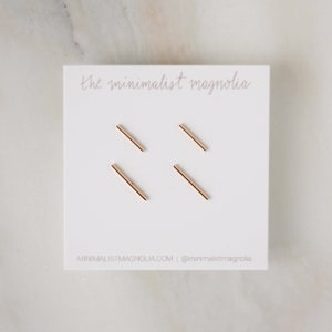 May include: Four gold bar earrings on a white card with the text "the minimalist magnolia" and "MINIMALISTMAGNOLIA.COM | @minimalistmagnolia".
