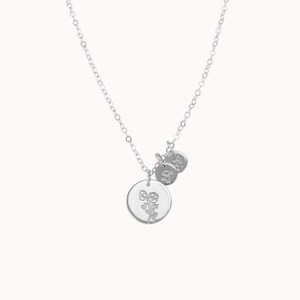 May include: A silver necklace with a delicate chain and three charms. The largest charm is a circle with a floral design. The two smaller charms are circles with a simple design.