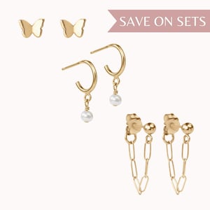 May include: Set of three gold earrings featuring a butterfly design, a hoop with a pearl drop, and a chain link design.  Save on Sets.