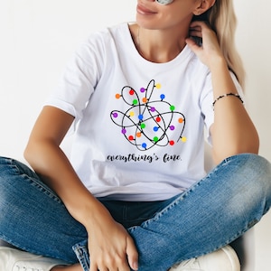 May include: White t-shirt with a tangled string of colorful Christmas lights and the text "everything's fine."