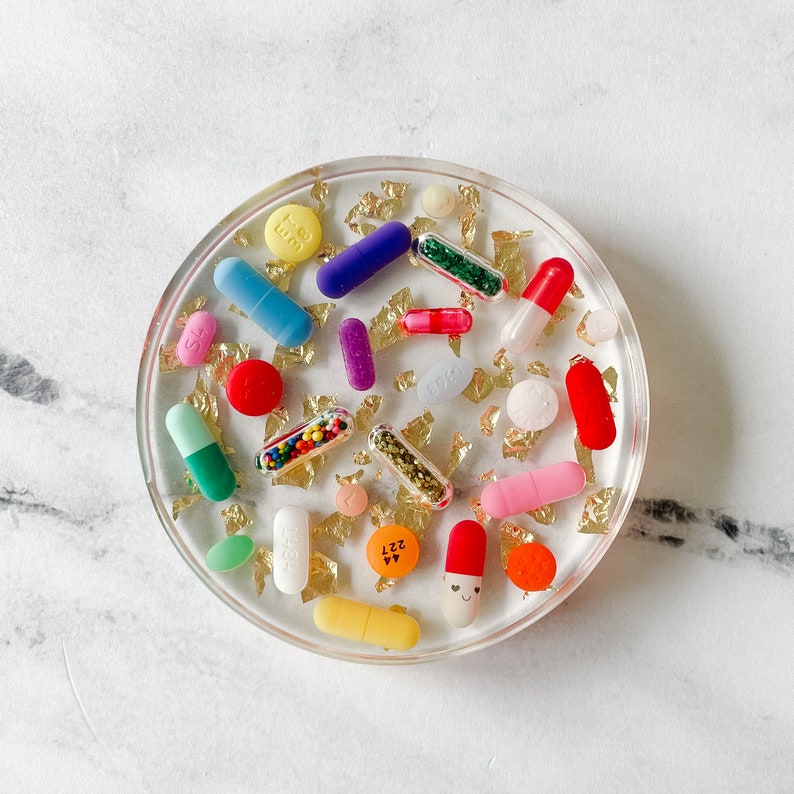 Clear, round resin coaster with flecks of gold leaf and colorful pills. All completed encased in resin. Some pills have glitter and sprinkles. Coasters are 4 inches in diameter.