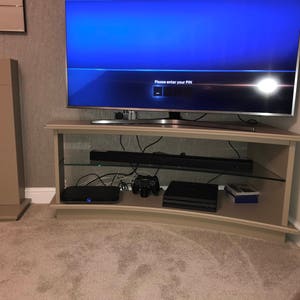 Puede incluir: Un centro de entretenimiento curvo con un televisor de pantalla plana, una barra de sonido y una consola de juegos. La pantalla del televisor muestra el mensaje "Por favor, ingrese su PIN".