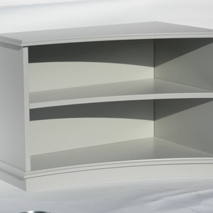 Puede incluir: Una estanter&iacute;a de madera gris curvada con dos estantes. Los estantes est&aacute;n curvados para coincidir con la forma de la estanter&iacute;a.