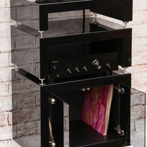May include: A black three-tiered stand with a turntable on the top shelf, an amplifier on the middle shelf, and a glass-door cabinet on the bottom shelf. The cabinet has a record album inside.