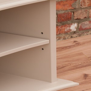 Puede incluir: Un mueble de TV de esquina con un acabado beige claro. El mueble tiene tres estantes y una base curva. El mueble est&aacute; hecho de madera y tiene un dise&ntilde;o simple y moderno.