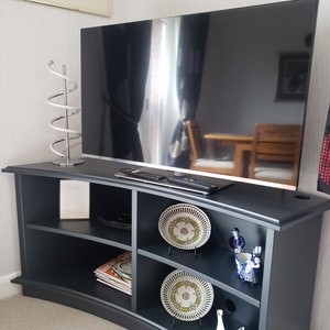 Puede incluir: Un centro de entretenimiento curvo negro con estantes, un televisor de pantalla plana y platos y figuritas decorativos.