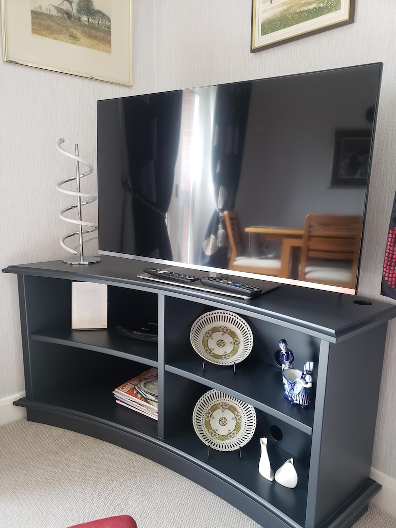 Puede incluir: Un centro de entretenimiento curvo negro con estantes, un televisor de pantalla plana y platos y figuritas decorativos.