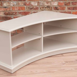 Puede incluir: Un centro de entretenimiento de madera blanca curvado con tres estantes. Los estantes est&aacute;n curvados para que coincidan con la forma de la unidad.
