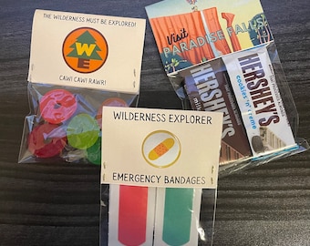May include: Three small gift bags with various items inside. The first bag contains red and green gummy candies and a card that says "The wilderness must be explored!" with a cartoon image of a tree and the letters "WE". The second bag contains a chocolate bar with the text "HERSHEY'S cookies 'n' creme" and a card with a cartoon image of a hot air balloon and the text "Visit Paradise Falls". The third bag contains two small bandages and a card with the text "Wilderness Explorer" and "Emergency Bandages".