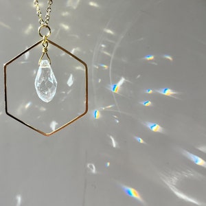 May include: A gold chain necklace with a hexagonal pendant that holds a clear quartz crystal.