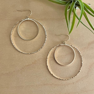 May include: A pair of gold-toned hoop earrings with a smaller circle inside the larger circle. The earrings have a textured finish.