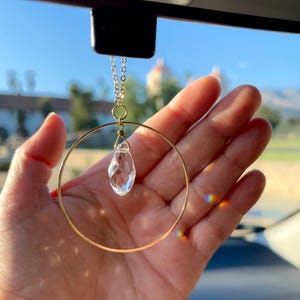 May include: A gold-toned hoop with a clear crystal pendant hanging from a rearview mirror.