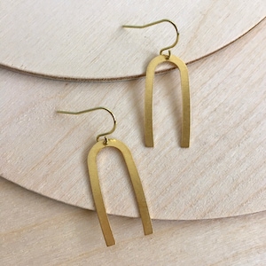 May include: A pair of gold-toned arch-shaped earrings with a simple design. The earrings are made of metal and have a hook closure.