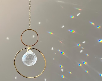 May include: A gold chain necklace with a clear crystal pendant hanging from two gold hoops.