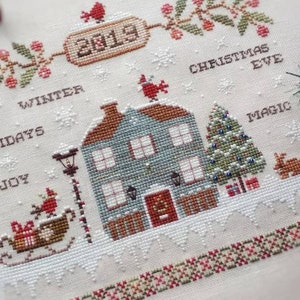 May include: A cross-stitch pattern featuring a winter scene with a house, a Christmas tree, a snowman, and the words "Winter Holidays Joy Christmas Eve Magic".