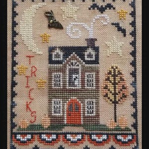 May include: Cross-stitch sampler featuring a house with a red door, a crescent moon, stars, and a bat charm. The word "TRICKS" is stitched vertically on the left. The design has a Halloween theme, with a decorative border and autumn colors.
