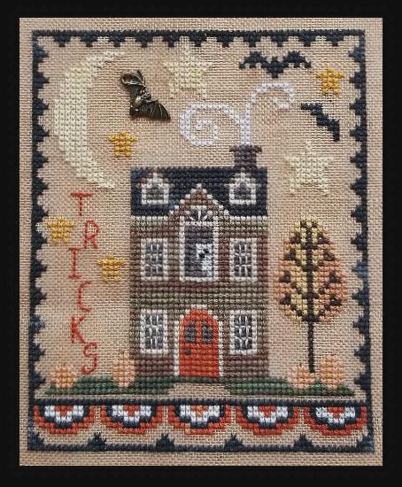 May include: Cross-stitch sampler featuring a house with a red door, a crescent moon, stars, and a bat charm. The word "TRICKS" is stitched vertically on the left. The design has a Halloween theme, with a decorative border and autumn colors.