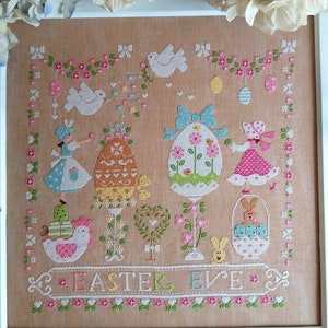 May include: A cross-stitch embroidery design featuring a pastel colored Easter scene with bunnies, birds, eggs, and flowers. The text "Easter Eve" is stitched in the bottom center of the design.