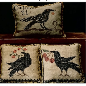 Puede incluir: Tres fundas de cojín bordadas con cuervos negros. La funda de cojín superior tiene el texto "October 31" bordado. Las dos fundas de cojín inferiores muestran cuervos con bayas rojas.