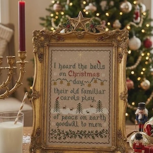 May include: A rectangular gold ornate frame containing a cross-stitch sampler with the text: I heard the bells on Christmas day, their old familiar carols play, of peace on earth goodwill to men. The design features small trees, deer, and bells.