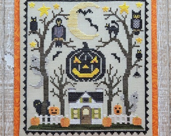 May include: A cross-stitch Halloween design featuring a spooky house, jack-o'-lanterns, bats, owls, and ghosts. The artwork is framed with an orange floral fabric border. The color palette includes black, yellow, orange, and gray.